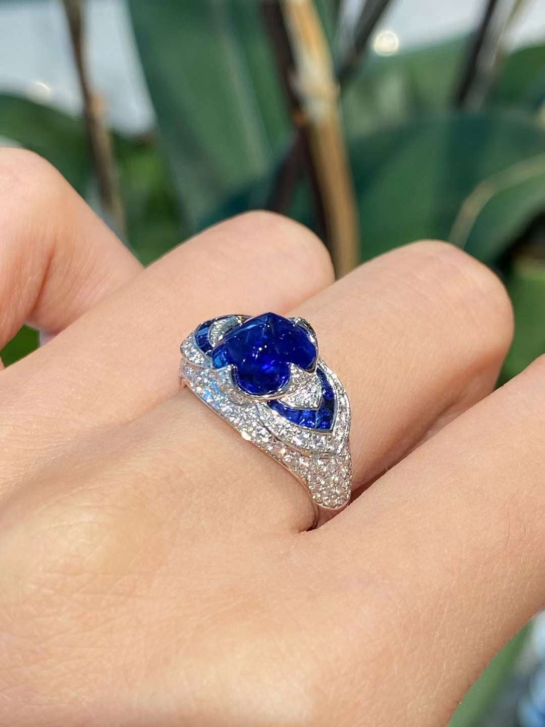 Angled perspective highlighting pavé diamond setting, dimensional marquise design, and deep blue sculpted floral center stone