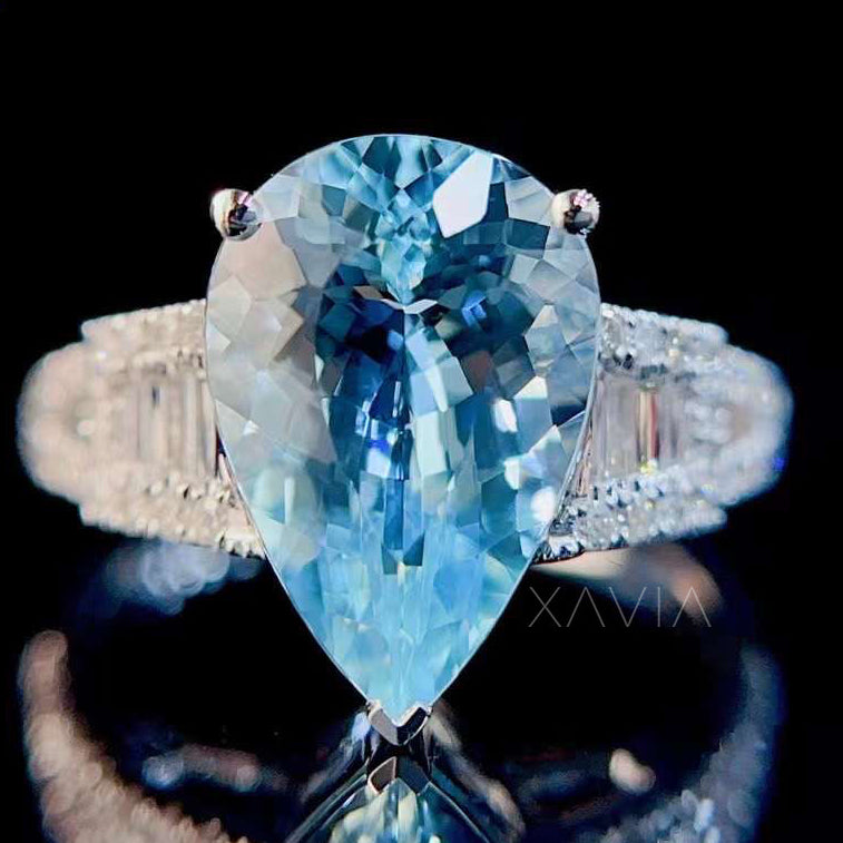 Luxury pear cut aquamarine engagement ring featuring baguette diamond halo and pavé split shank setting photographed in studio lighting with reflective black surface