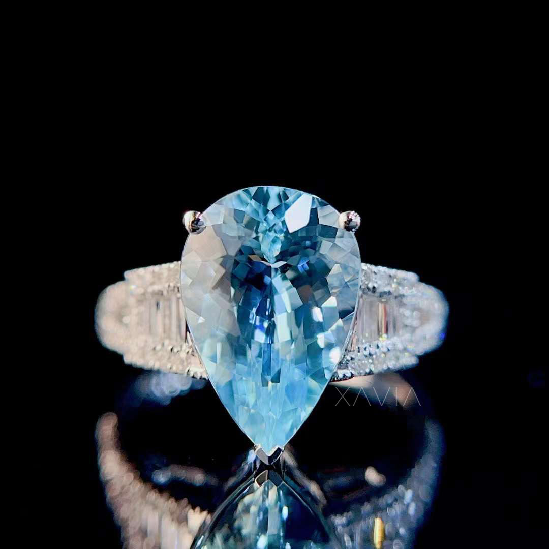 Close-up front view of large pear aquamarine gemstone ring with bright blue color and sparkling baguette diamond halo design
