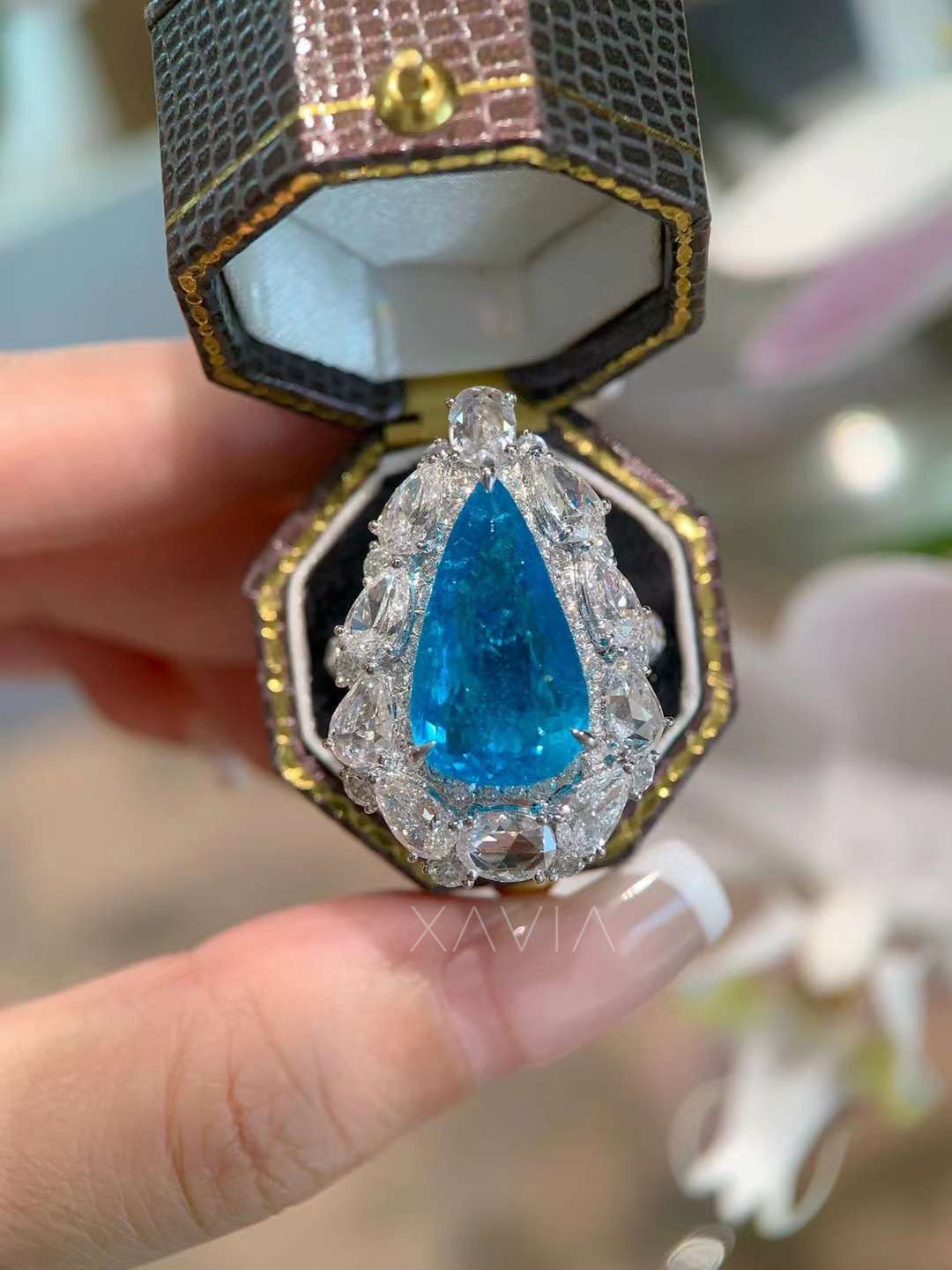 Luxury pear cut vivid blue gemstone cocktail ring surrounded by marquise, oval and round lab grown diamonds forming dramatic halo cluster setting in fine jewelry presentation box