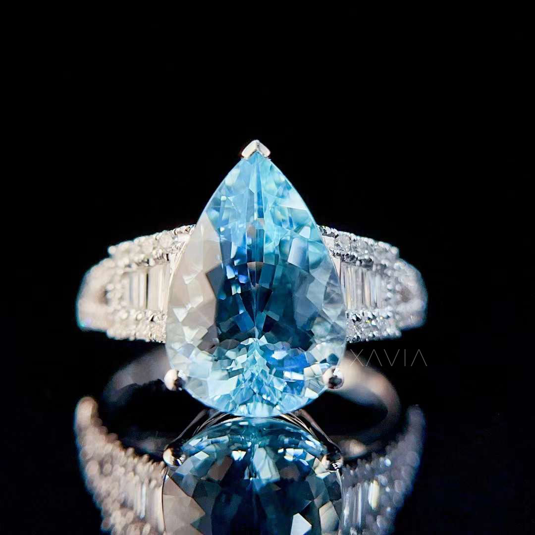 Front view of pear cut aquamarine ring surrounded by baguette diamonds and pavé accents in luxury bridal setting with mirror reflection background