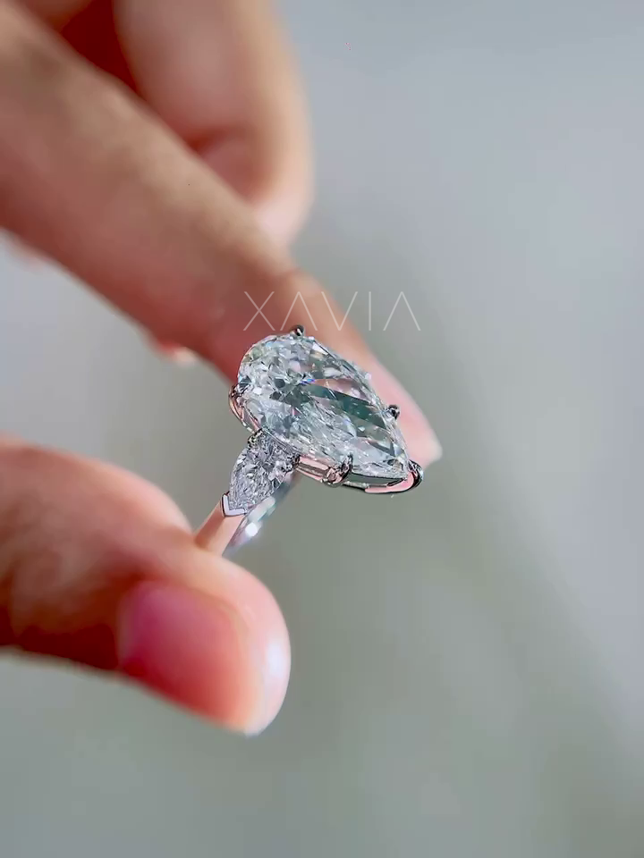 angled close-up of pear cut lab grown diamond engagement ring featuring trillion side diamonds in elevated prong setting held between fingers