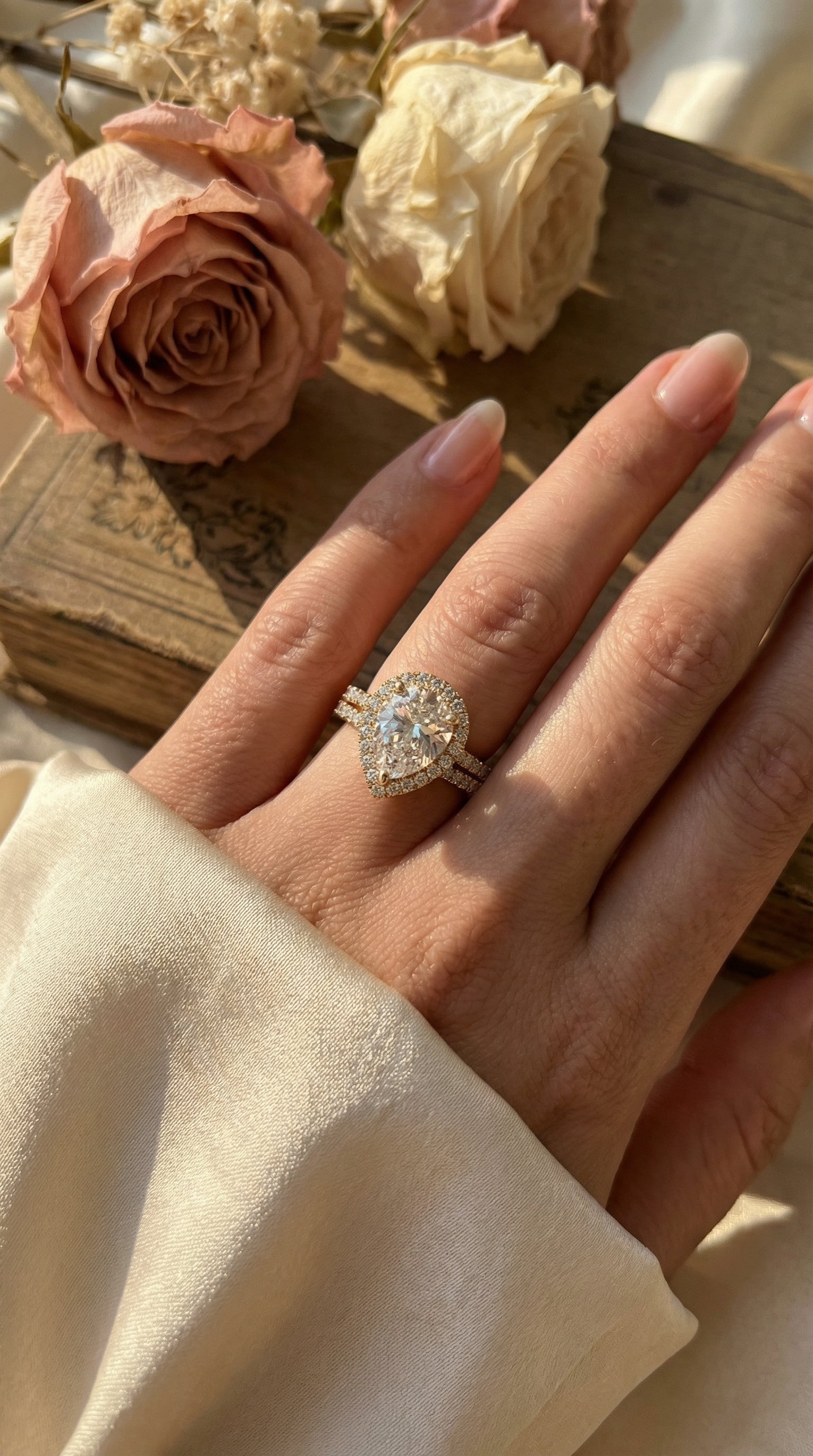 Pear shaped lab diamond halo engagement ring worn on hand in natural sunlight with pavé 
