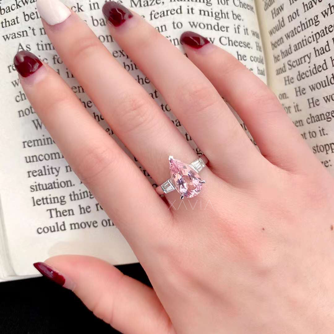 Elegant pear cut blush pink morganite ring worn on hand featuring tapered baguette diamond side stones and refined minimalist white gold band