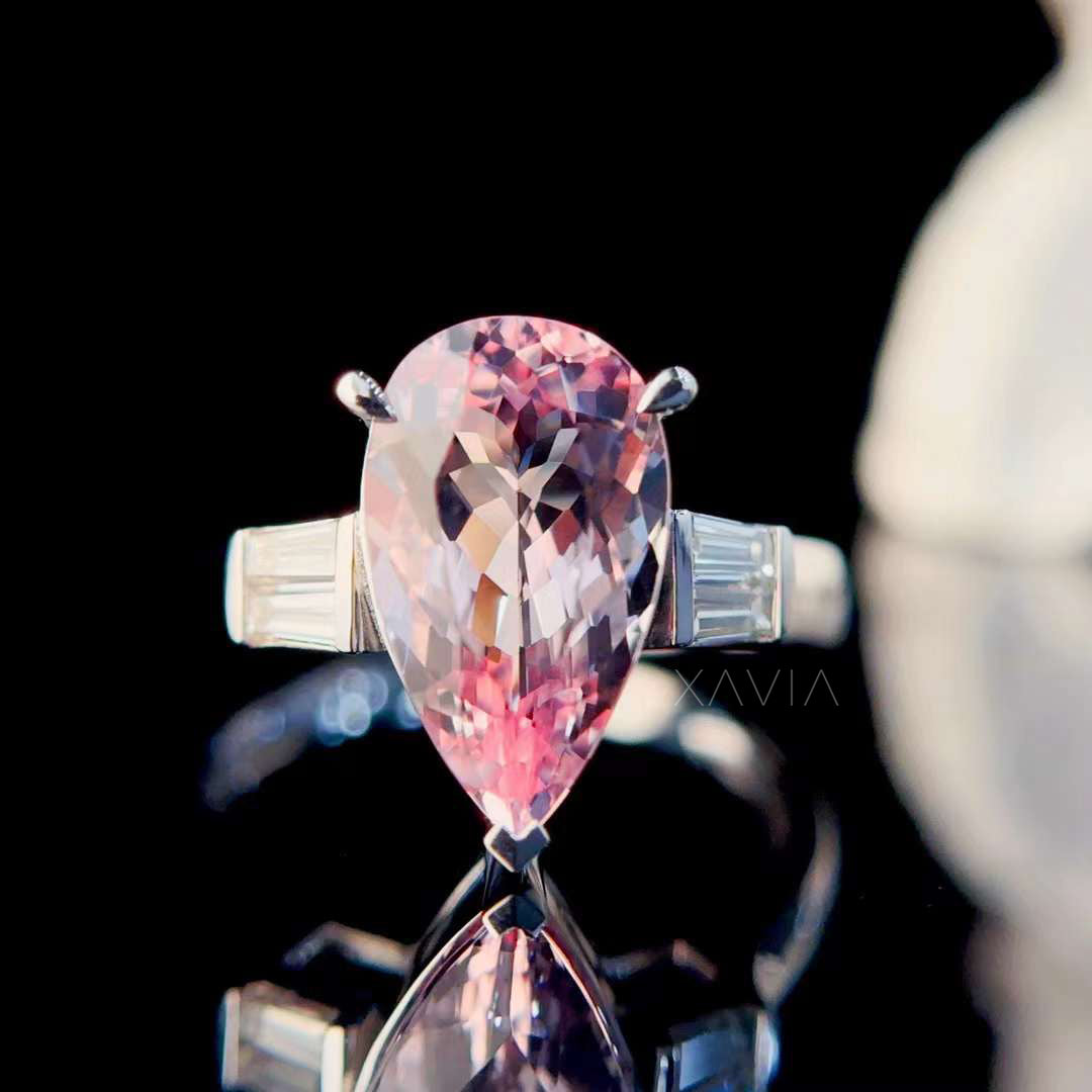 Side profile of pear cut morganite three stone ring showing elevated basket setting and tapered baguette diamond accents in polished white gold