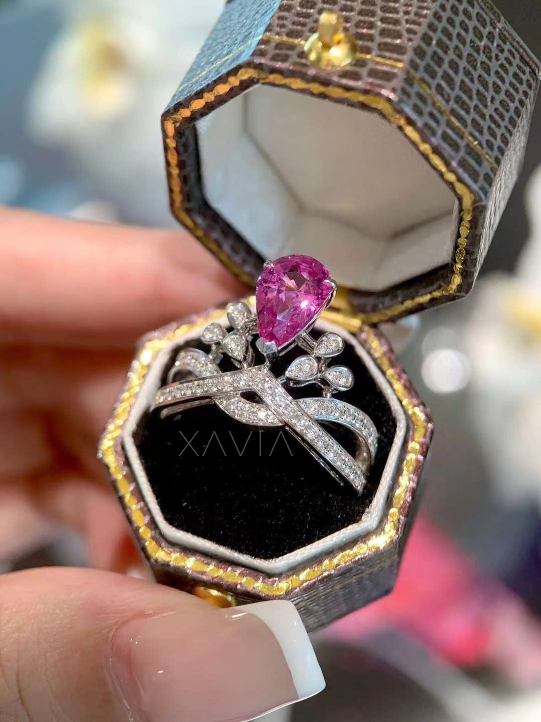 Diamond ring with a pink gemstone in an open jewelry box held by a hand.
