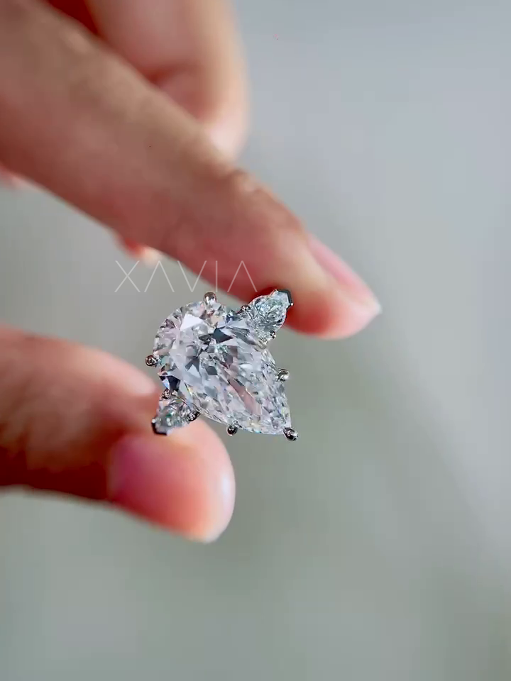 elegant pear cut lab grown diamond three stone engagement ring with trillion side diamonds displayed between fingers in soft natural lighting