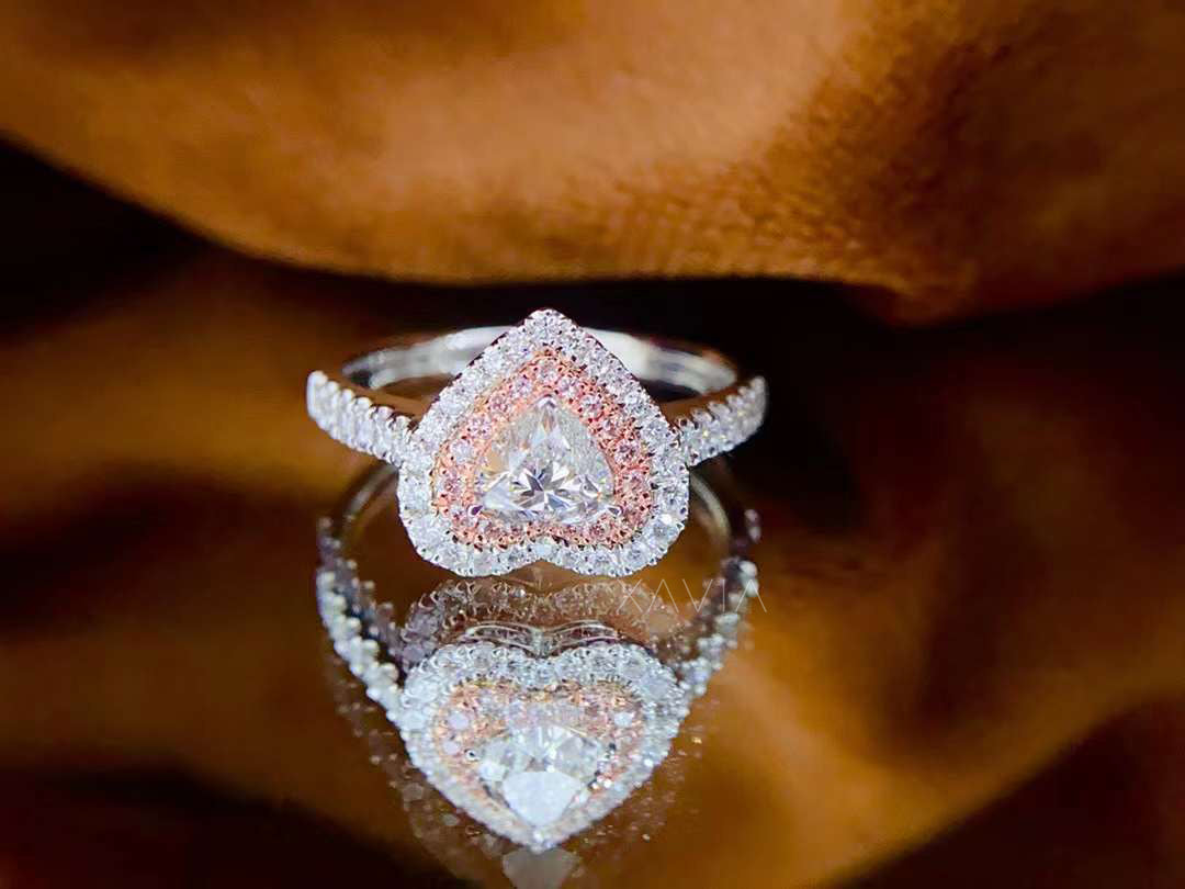 Heart cut lab-grown diamond ring with pink inner halo and outer white diamond halo, pavé band, showcased on golden-brown fabric