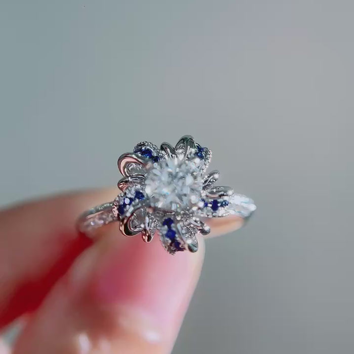 Round brilliant lab-grown diamond center framed by sculptural sapphire petal halo, pavé diamond shank and DEF VVS–VS clarity diamonds in solid gold.