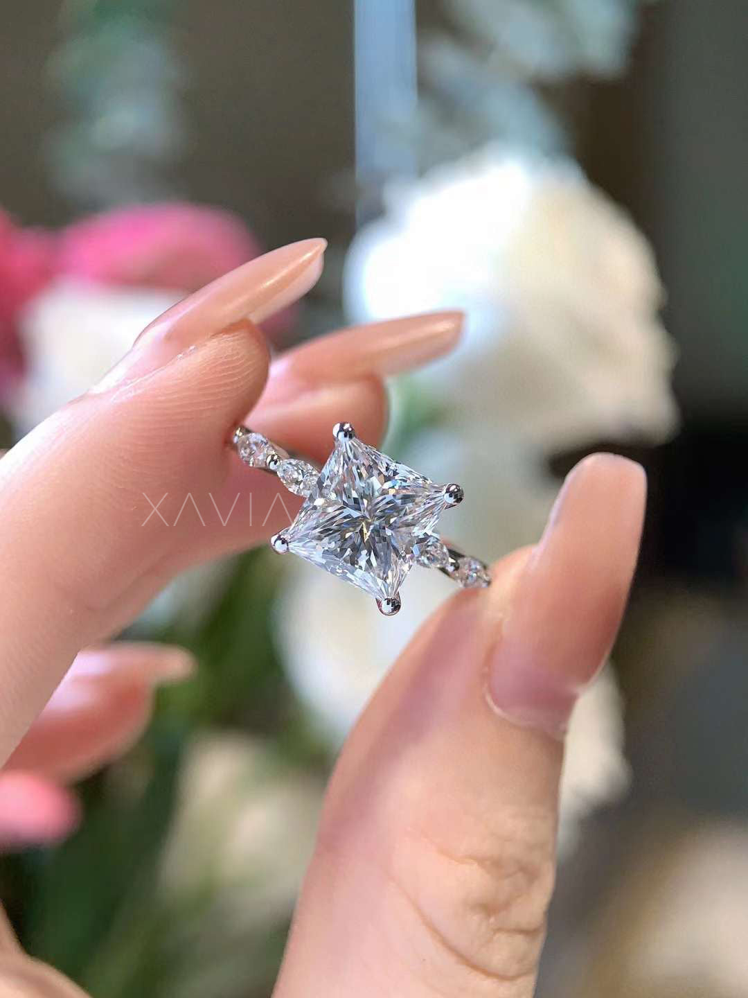 Close-up top view of a princess cut lab-grown diamond engagement ring featuring marquise accent diamonds along the band in a four-prong solitaire setting held between fingers