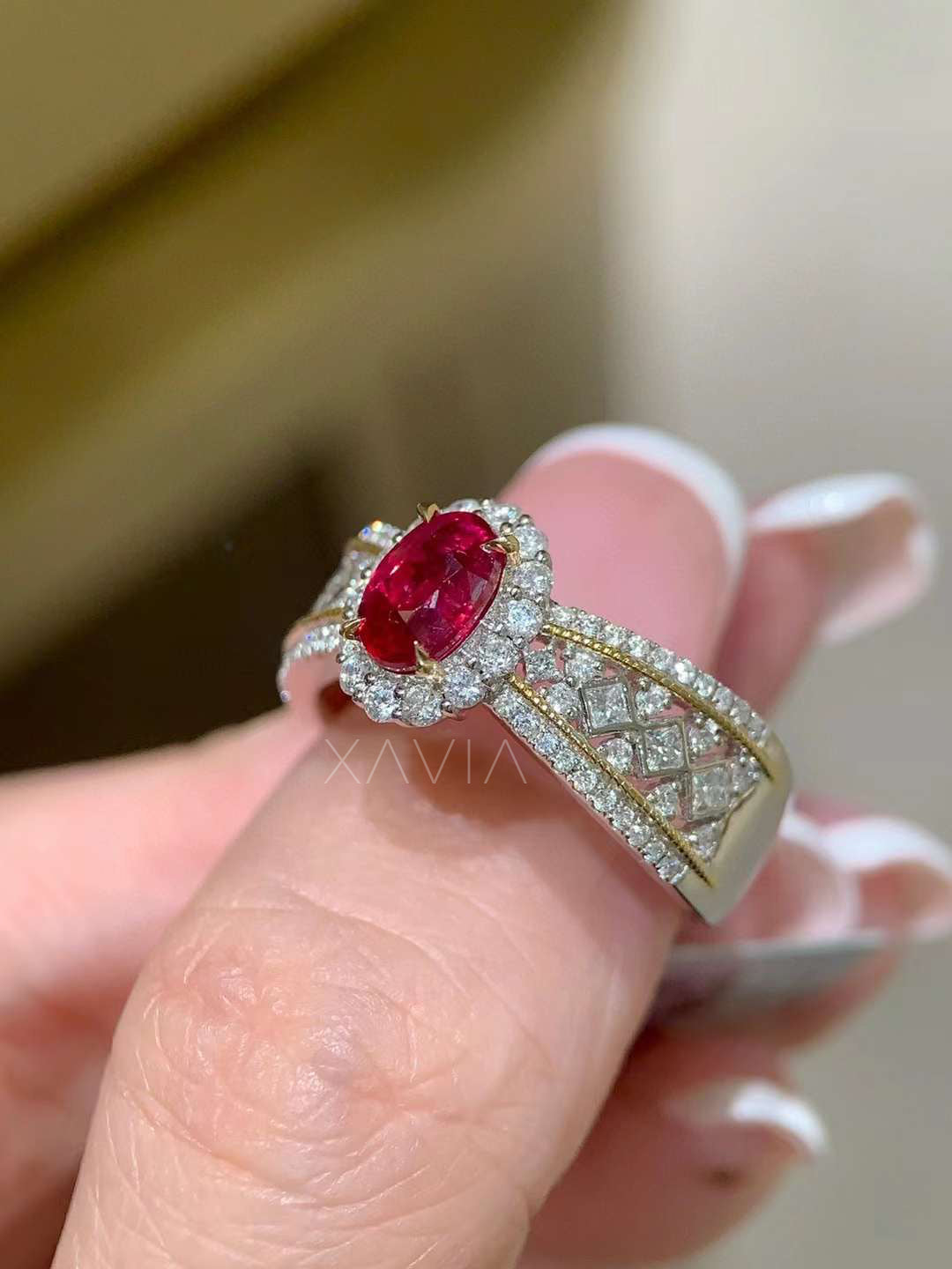 Elegant oval red gemstone halo ring worn on hand featuring diamond halo, split pavé band and decorative lattice diamond shoulders in luxury solid gold