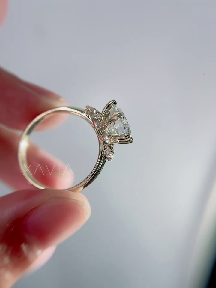 Close up view of round lab grown diamond engagement ring held between fingers showcasing cathedral setting crescent halo detail and floral diamond accents