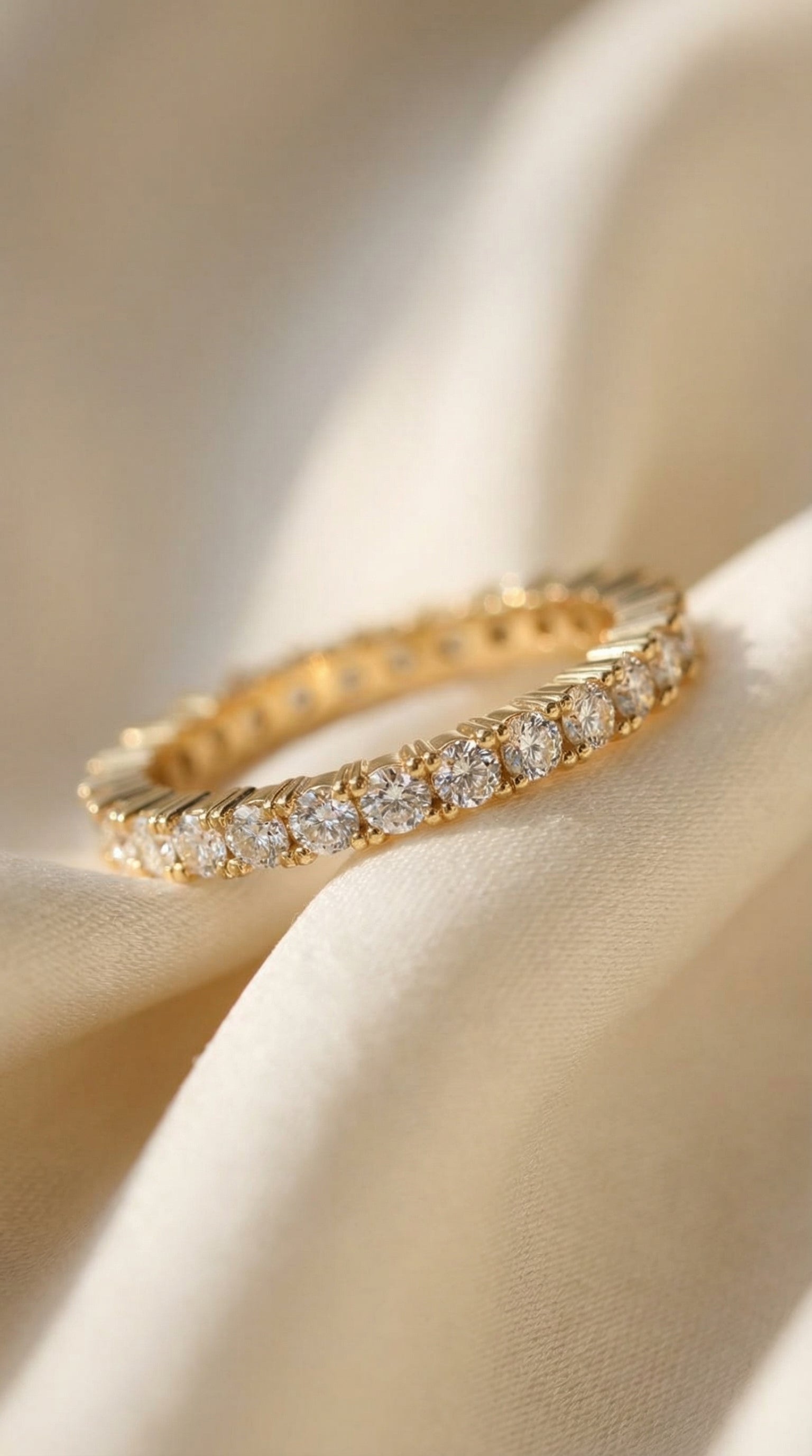 close angled image of round brilliant lab grown diamond eternity band ring resting on soft silk fabric highlighting brilliant diamonds and polished yellow gold fluted structure
