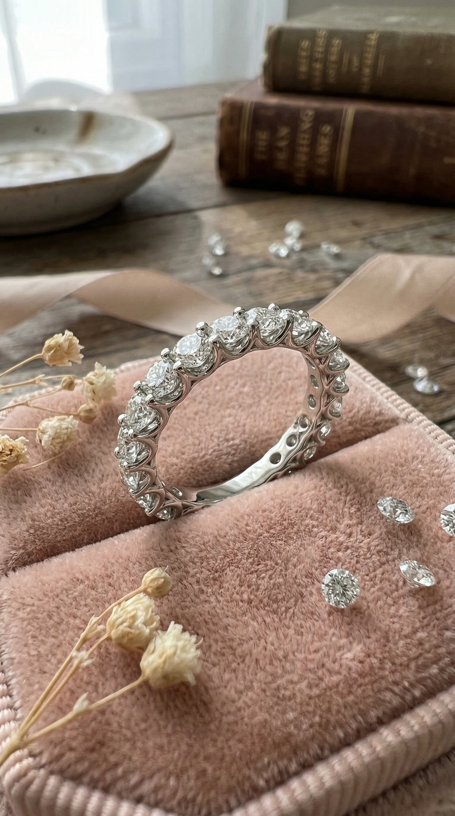 round brilliant lab grown diamond eternity band ring displayed on blush velvet fabric with loose diamonds and soft romantic background lighting