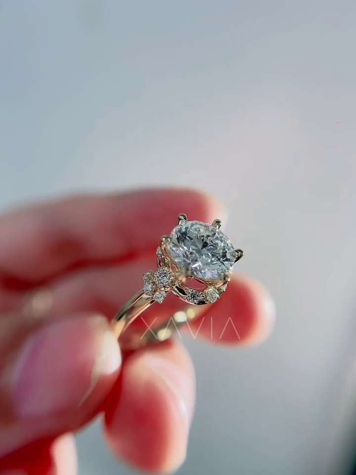 Close angled shot of round lab diamond engagement ring with sculpted crescent halo under gallery and clustered round diamond accents near shoulders