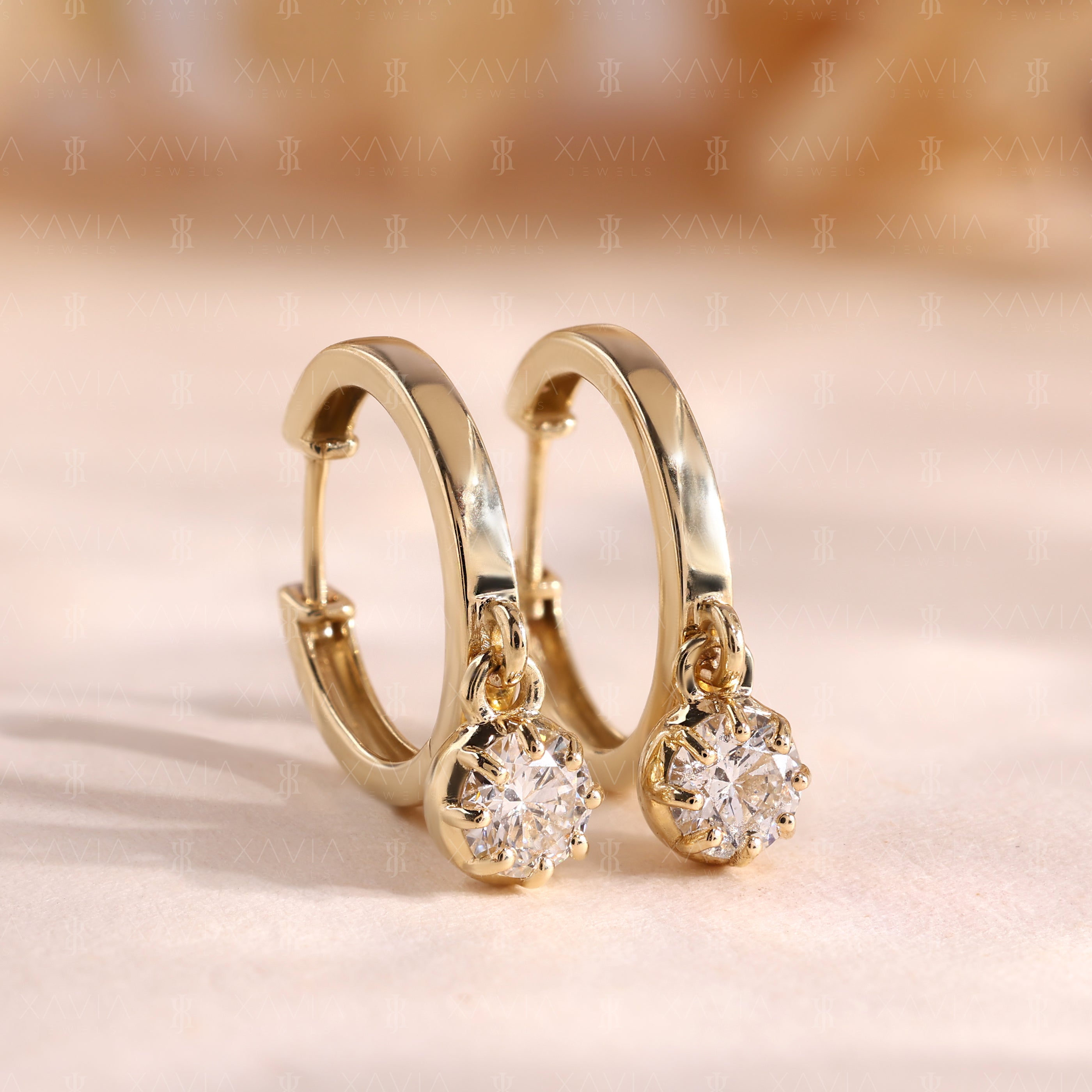 Angled close-up view of polished yellow gold huggie hoop earrings featuring round brilliant lab-grown diamond solitaire dangle drops with elegant floating 