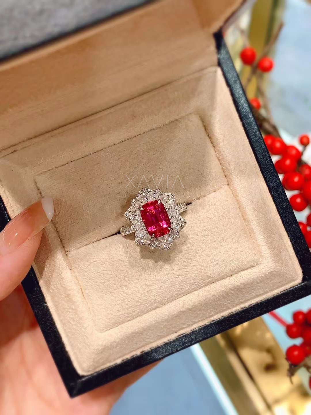 Cushion-cut ruby cocktail ring with brilliant diamond halo worn elegantly on hand with festive red berries