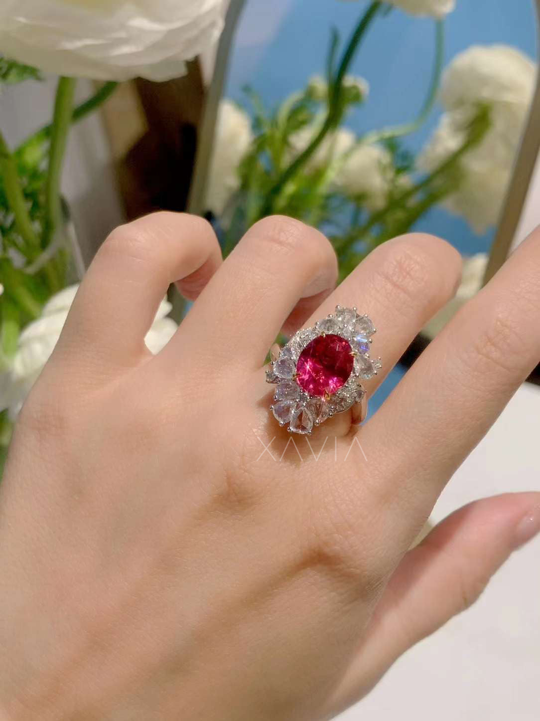 Hand shot of luxury ruby and diamond halo cocktail ring with oval ruby and clustered marquise accents