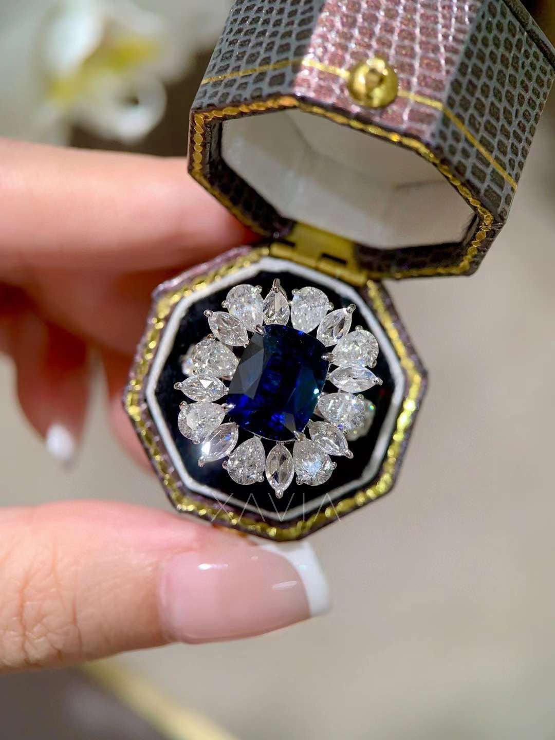 Close-up angled view of royal blue cushion sapphire surrounded by alternating pear and marquise lab diamonds arranged in floral halo cluster cocktail ring design