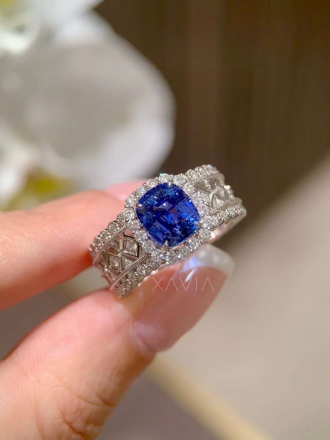 angled perspective of cushion blue sapphire halo ring showing intricate diamond lattice band design with pavé diamond edges in high polish white gold