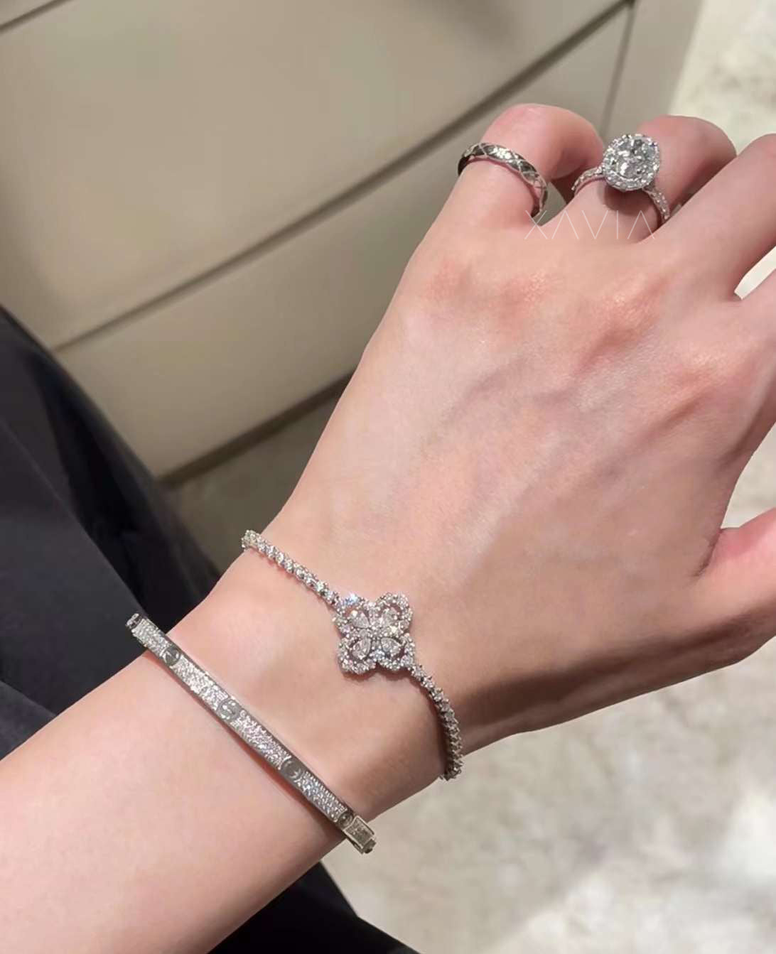 Side angle view of oval cut halo lab-grown diamond ring with pavé shank, worn with stacked designer bracelets