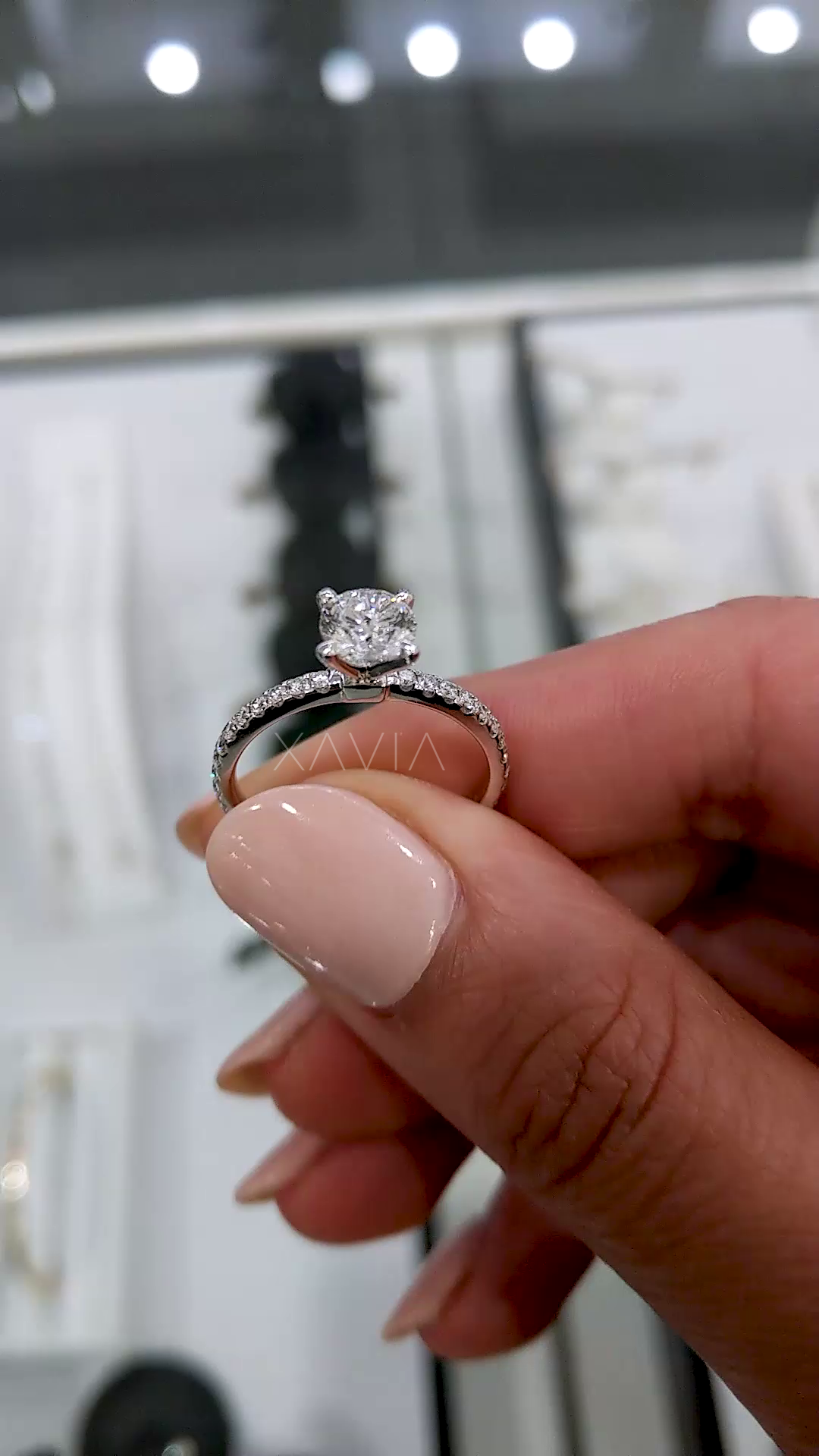 detailed handheld view of round lab diamond engagement ring showing prong setting, thin pavé band and high polish finish in luxury jewelry setting