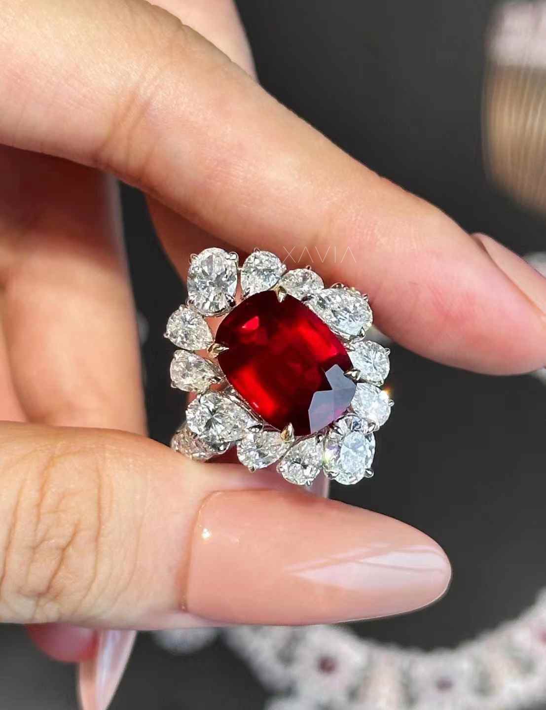 Statement cushion cut ruby red halo diamond ring photographed on model’s hand emphasizing scale, sparkle, and luxury finish