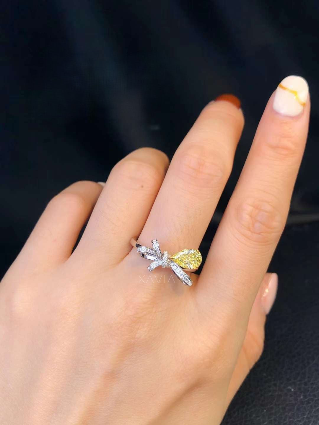 fancy yellow pear cut diamond bow engagement ring with pavé-set accents, worn on hand, elegant luxury jewelry style