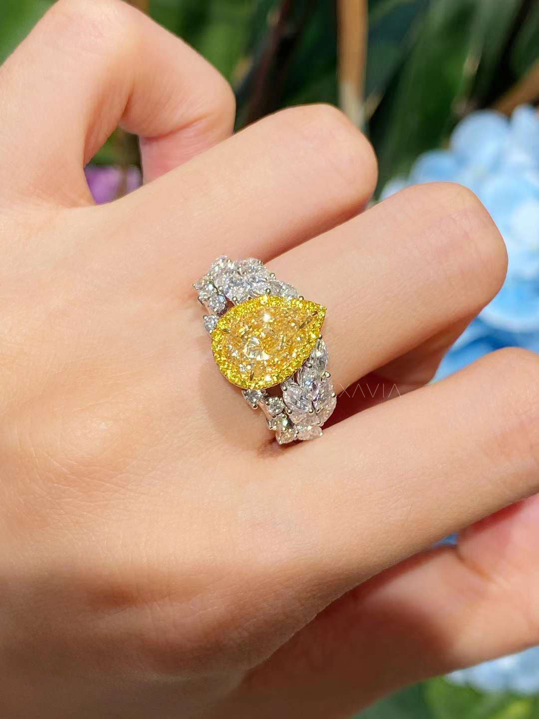 close-up of fancy yellow pear diamond ring with pavé halo and leaf-like white diamond band, worn on hand in natural light